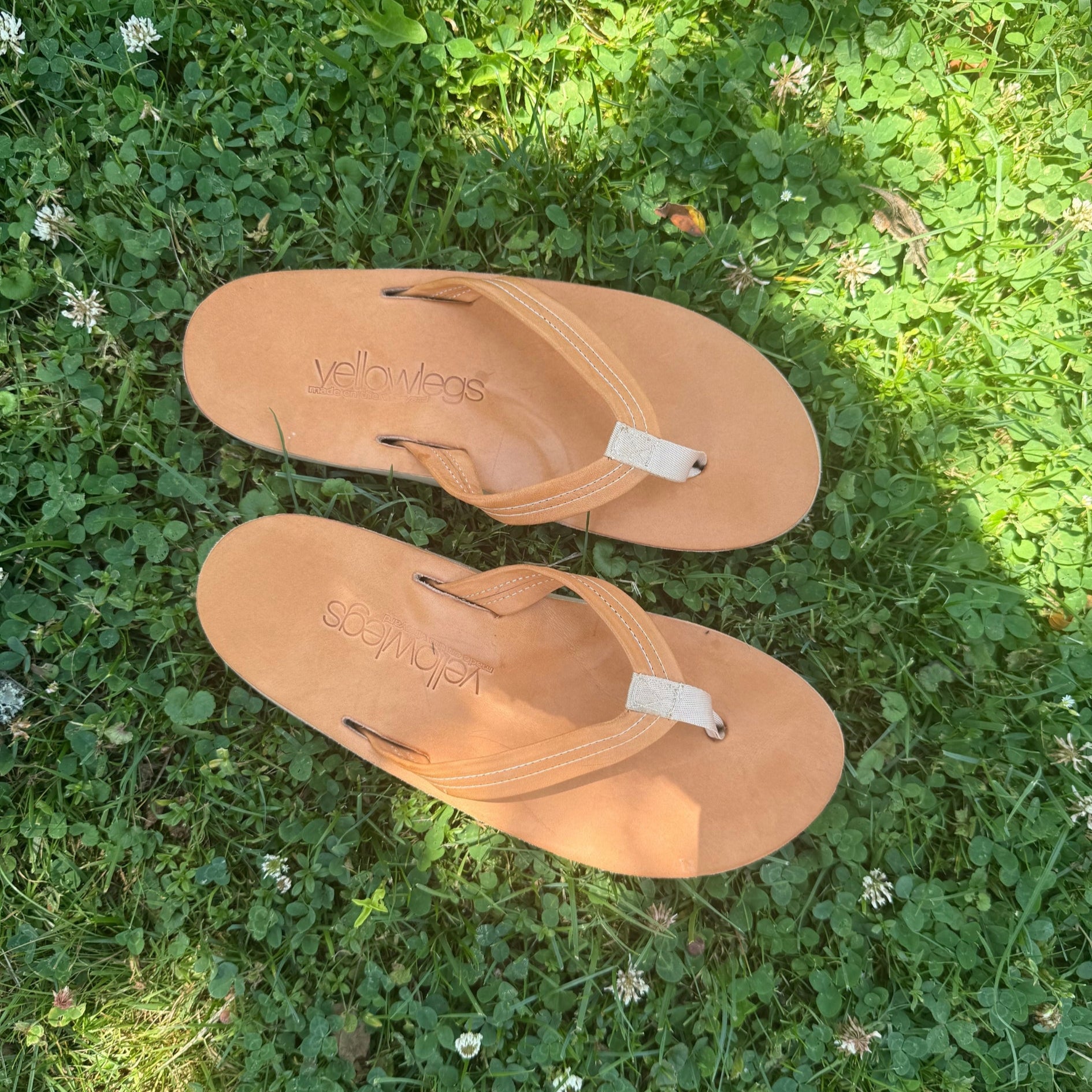 Pair of handmade tan leather sandals on a grassy background